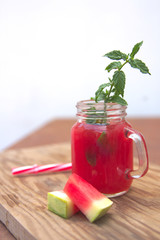 Glass jar with watermelon juice with a sprig of green mint and small segments of watermelon