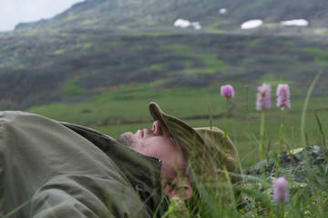 tired traveler in the mountains - a man in a hat and travel clothes resting, lying on his back in...