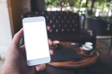 Mockup image of hand holding white mobile phone with blank desktop screen in cafe
