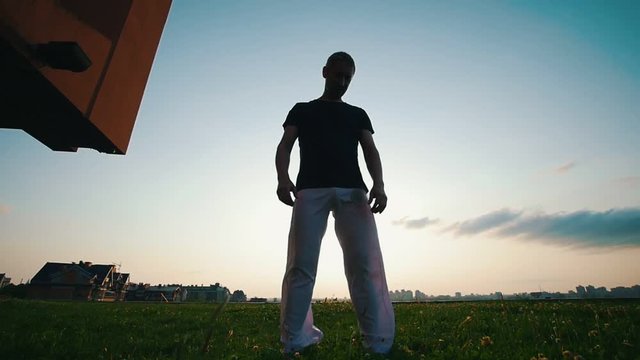 Athletic man standing against the sky, his white wide pants fluttering in the wind