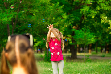 Obraz premium Young mother and little daughter playing in park with soap bubbles. Love family, parenthood, childhood