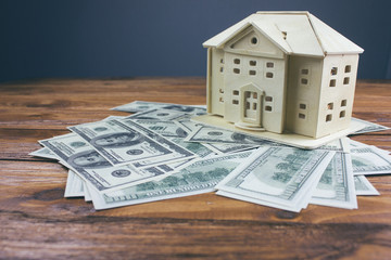 ..Model of house with dollar bill on wooden table.