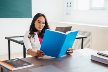 Young woman sitting by table and reading book.