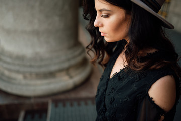 Obraz na płótnie Canvas Young beautiful stylish girl goes in a black dress in the city. Outdoor summer portrait of a young woman with a hat