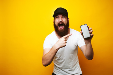 Amazed screaming young bearded man pointing at smartphone
