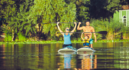 positive smiling boy in rashguard and his young father enjoying stand up paddleboarding