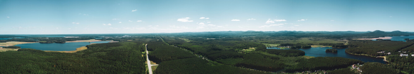 Aerial drone panoramic view of the land of lakes landscape, the road among the deep mixed forest, mountains on the background, long panoramic photo in summer evening in South Ural, Russia