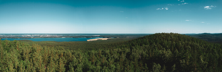 Fototapeta na wymiar Aerial drone panoramic view of mountain peak with thin high tree trunks, mixed forest of birches and pine trees, lakes on the background, mountain Sugoyak, South Ural, Russia
