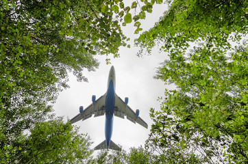 big blue passenger aircraft delivers passengers and cargo, lands in the airport, wide view of owerflying above in a hole between forest trees in front of the cloudy sky background