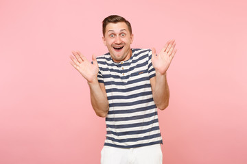 Fototapeta premium Portrait of cheerful surprised young hipster man dresssed casually in striped t-shirt spreading hands isolated on trending pink background. People sincere emotions, youth lifestyle concept. Copy space