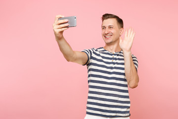 Portrait of smiling young man wearing striped t-shirt doing selfie shot on modern mobile phone...