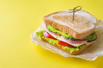 Sandwich with cheese, ham and fresh vegetables on a yellow bright background.