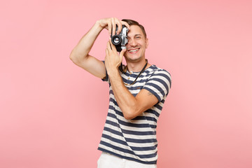 Portrait of smiling young photographer man wearing striped t-shirt take pictures on retro vintage photo camera isolated on trending pastel pink background. People sincere emotions lifestyle concept.