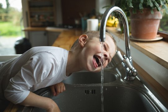 Boy drinking water from faucet in kitchen
