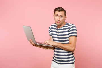 Portrait of concentrated young man in striped t-shirt working on laptop computer, copy space isolated on trending pastel pink background. People sincere emotions lifestyle concept. Advertising area.