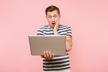 Portrait of sad upset young man wearing striped t-shirt working on laptop computer, copy space isolated on trending pastel pink background. People sincere emotions lifestyle concept. Advertising area.