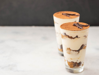Homemade tiramisu, traditional Italian dessert in glass on white table. Copy space.