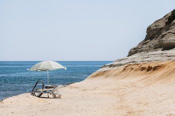 Two blue deck chairs with a beach umbrella with green stripes in Malta / Two blue deck chairs with a beach umbrella with green stripes in a lonely beach.