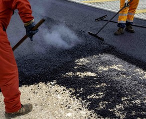Worker distributes on the edge the asphalt laid out for the construction of a road