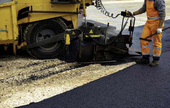 Workers regulate tracked paver laying asphalt heated to temperatures above 160 ° pavement on a runway