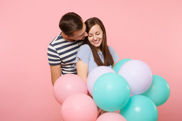 Fototapeta na wymiar Portrait of young happy tender couple in love. Woman and man in blue clothes celebrating birthday holiday party on pastel pink background with colorful air balloons. People sincere emotions concept.