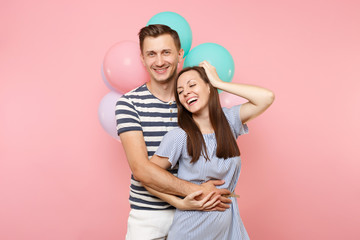 Portrait of young happy smiling couple in love. Woman and man in blue clothes celebrating birthday holiday party on pastel pink background with colorful air balloons. People sincere emotions concept.