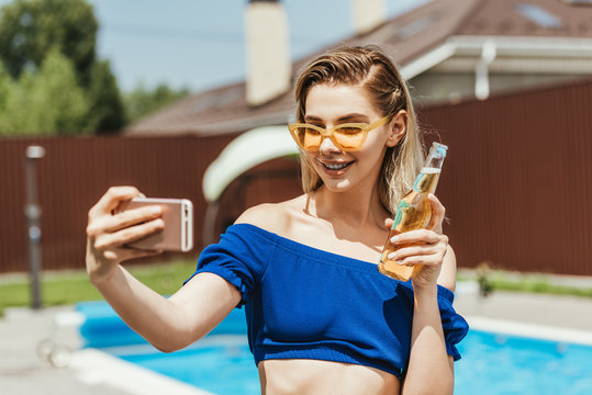happy attractive girl taking selfie with bottle of beer on smartphone - Powered by Adobe