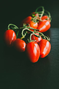 Macro of glossy red tomatoes against black shale background
