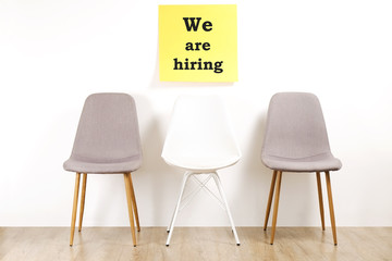 Job recruitment advertisement, WE ARE HIRING text written on yellow wall poster, three empty loft style chairs. Human resources campaign to find workers for vacant job. Close up, copy space background