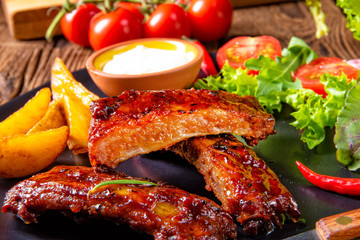 bbq spareribs on the plate with green salad and white sauce.