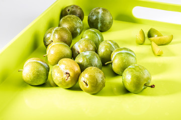 Delicious green plums fresh and raw claudias in wicker basket. On green background color.