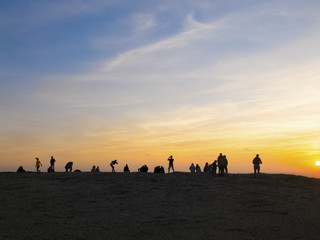 group of people in silhouette enjoy a colorful amazing sunset on the rocks. men and woman in outdoor leisure activity. vacation and see the world concept