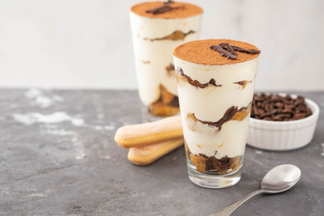 Tiramisu in a glass with coffee beans on grey background. Copy space. Selective focus.