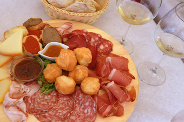 Heerlijk Toscaans voorgerechtbord met ham, kaas, salami, sauzen en coccoli evenals broodmand en wijn