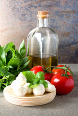 Small balls of mozzarella with basil leaves, tomato and olive oil on rustic background