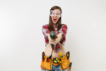 Strong young energy handyman woman in plaid top shirt denim shorts kit tools belt full of instruments in protective goggles hold power electric drill isolated on white background. Female in male work.