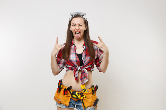 Strong excited handyman woman in plaid top shirt, denim shorts, kit tools belt full of instruments in protective goggles isolated on white background. Female in male work. Copy space for advertisement