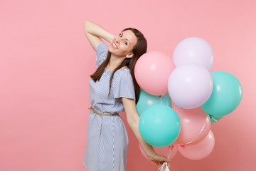Fototapeta na wymiar Portrait of pretty smiling young woman in blue dress holding colorful air balloons keeping hand near head isolated on bright pink background. Birthday holiday party, people sincere emotions concept.