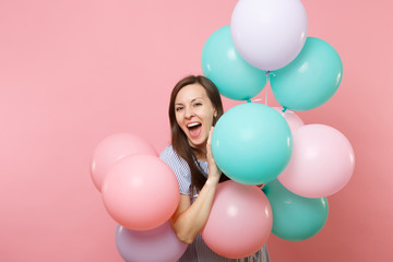Fototapeta na wymiar Portrait of joyful young happy woman with opened mouth in blue dress holding colorful air balloons isolated on bright trending pink background. Birthday holiday party, people sincere emotions concept.