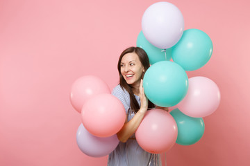 Fototapeta na wymiar Portrait of pretty smiling young woman in blue dress holding colorful air balloons look aside on copy space isolated on bright pink background. Birthday holiday party, people sincere emotions concept.
