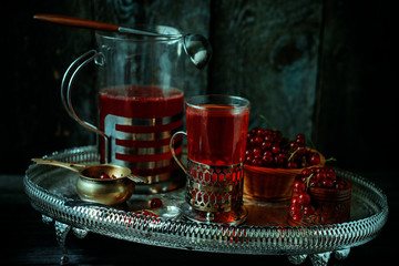 Still life in vintage royal style. Glass with red current tea or fruit-drink on silver dishes and tray