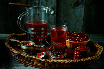 Still life in vintage style. Glass and decanter with red current tea or fruit-drink on wicker tray