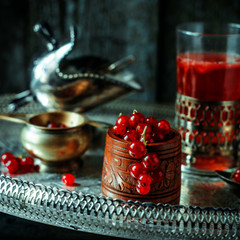 Still life in vintage royal style. Close up red current into wooden bowl and tea or fruit-drink on silver tray