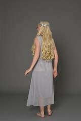full length portrait of blonde girl wearing dress and crown. standing pose with back to the camera. grey studio background. © faestock