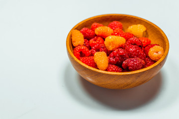 Close up little basket with red and yellow raspberries on white background