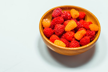 Close up little basket with red and yellow raspberries on white background. Top view
