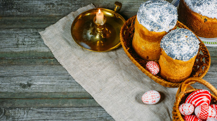 Red easter eggs with folk Ukrainian pattern lay into basket beside easter cakes and candlestick on sheet of vintage cloth on old wood background. Top view
