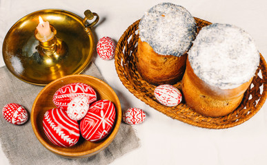 Red easter eggs with folk Ukrainian pattern lay into wood bowl beside easter cakes on white background. Top view.
