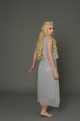 full length portrait of blonde girl wearing dress and crown. standing pose with back to the camera. grey studio background.