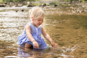Little girl is playing with water in a river.